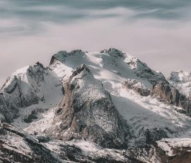 Snow-covered mountain range under cloudy sky Snowy mountain peaks with cloudy sky
